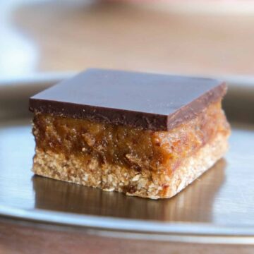 Sugar free miso tahini caramel slice with glossy dark chocolate topping on a plate.