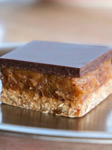 Sugar free miso tahini caramel slice with glossy dark chocolate topping on a plate.