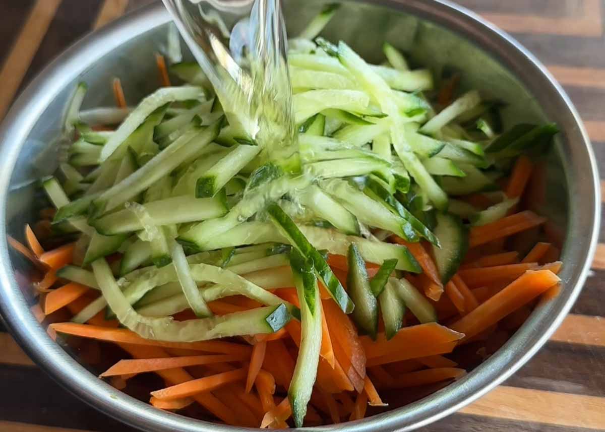 Julienned carrot and cucumber being mixed together for quick pickled vegetables.