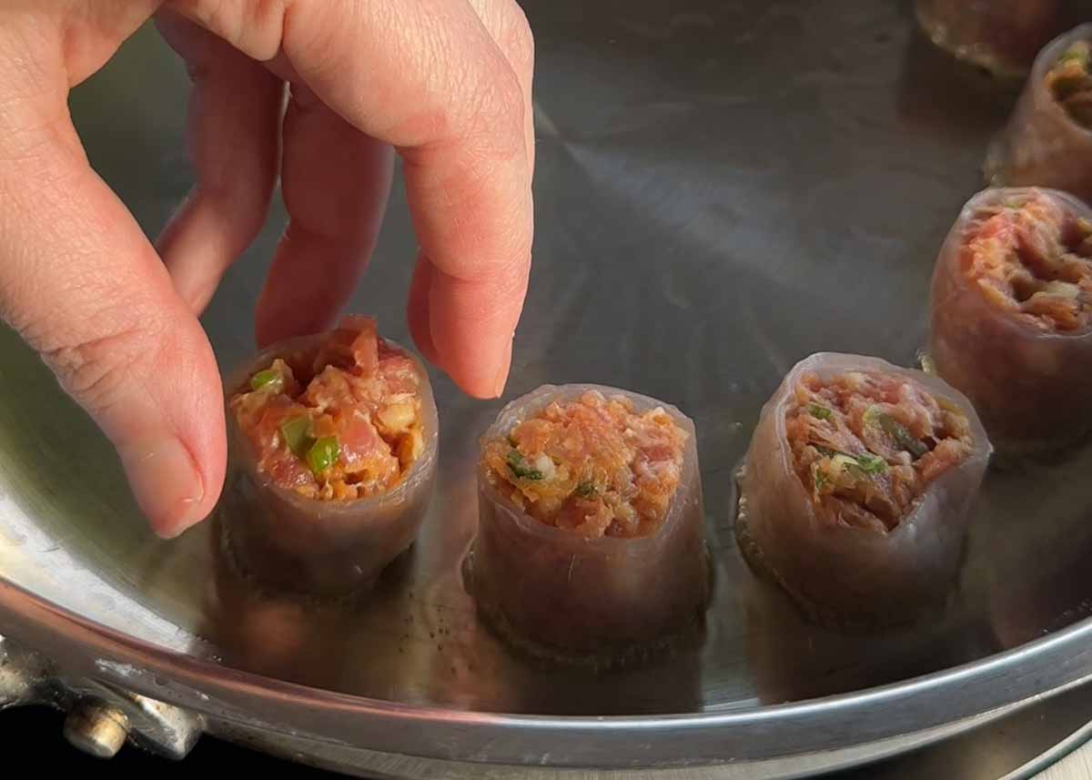 Placing sliced pork rice paper dumplings into a frying pan for cooking.