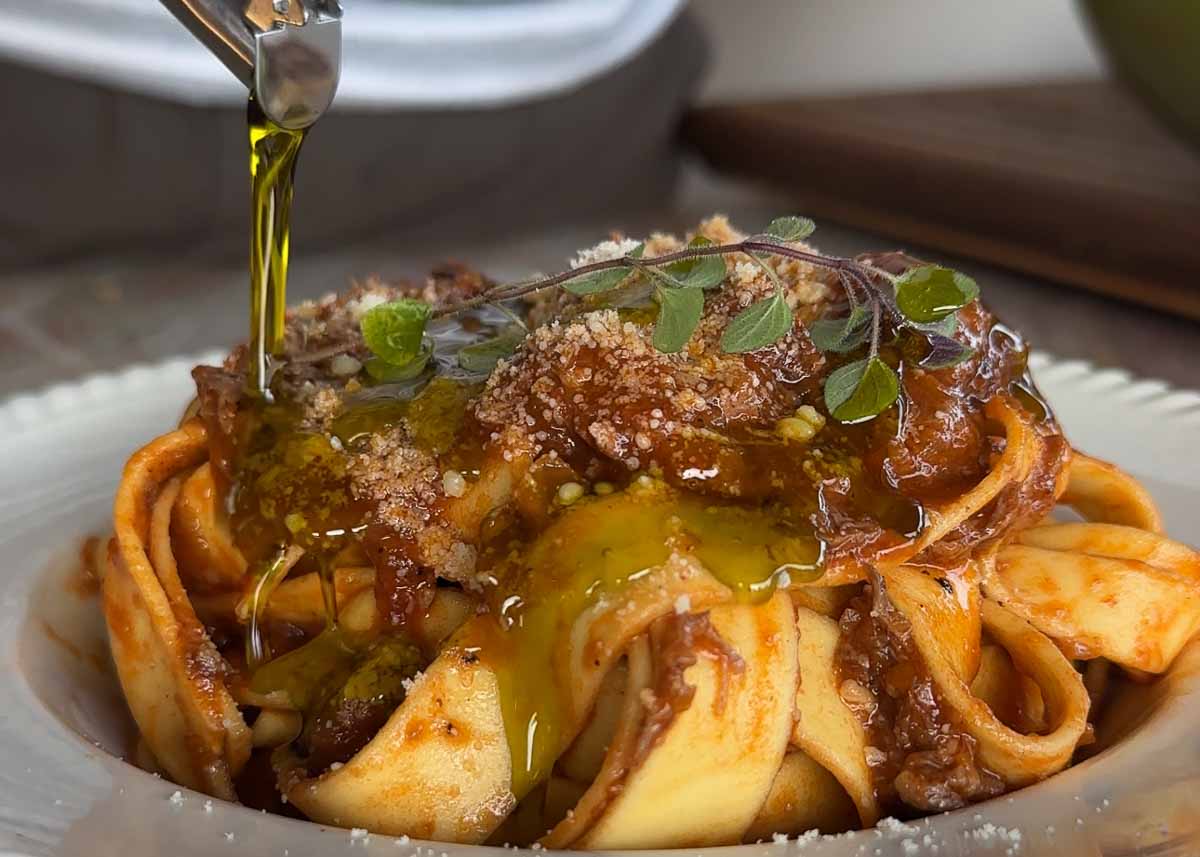 Boneless lamb shank rosé ragu being plated and finished with olive oil drizzle