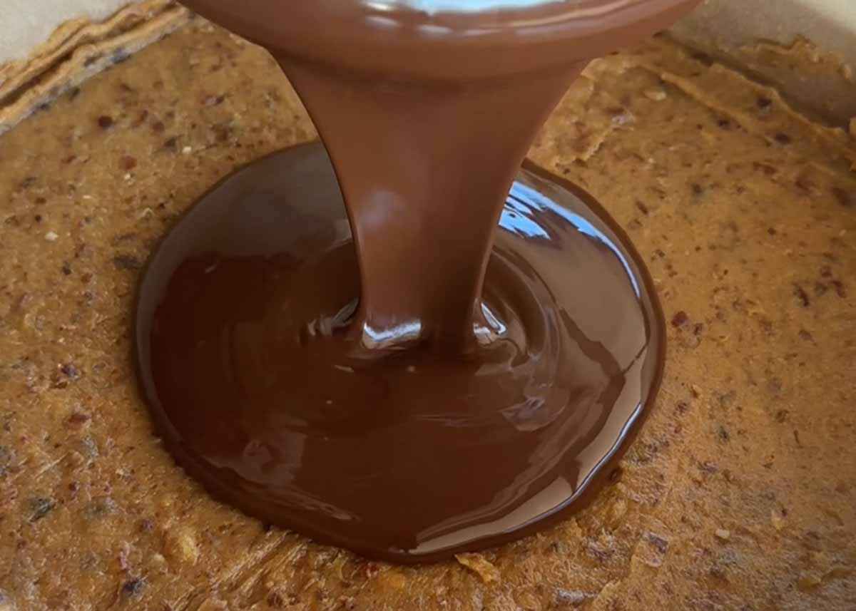 Pouring melted dark chocolate over the caramel layer.