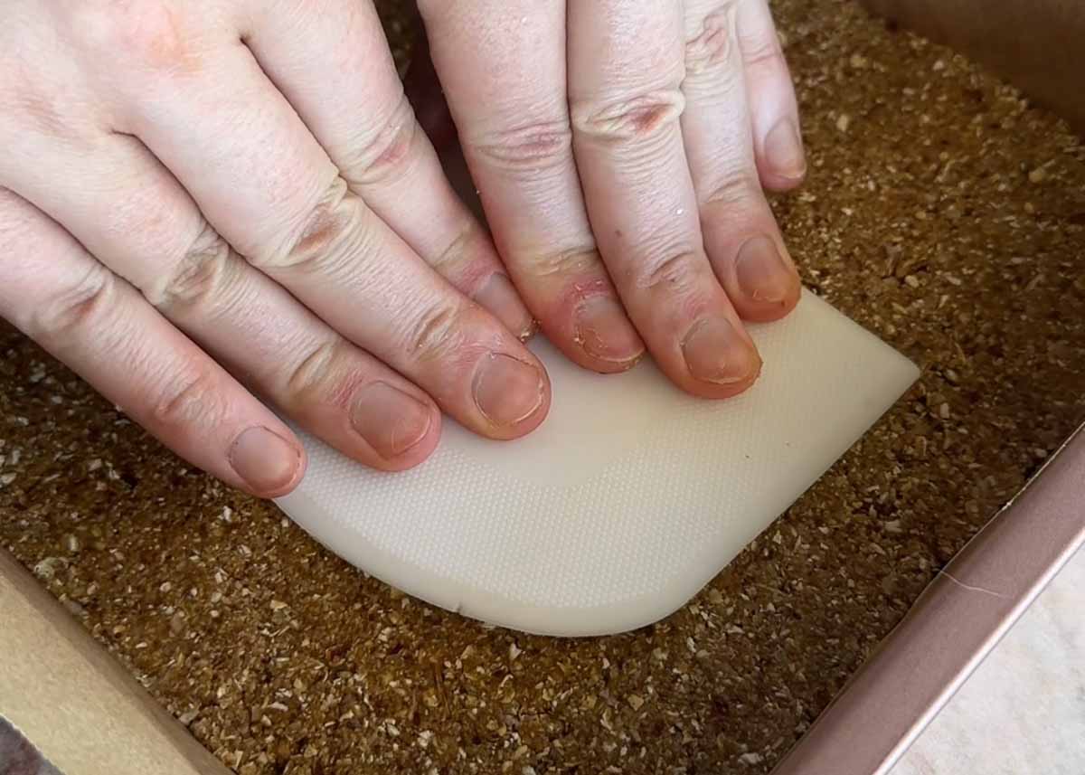 Pressing the oat base into a lined baking tray.