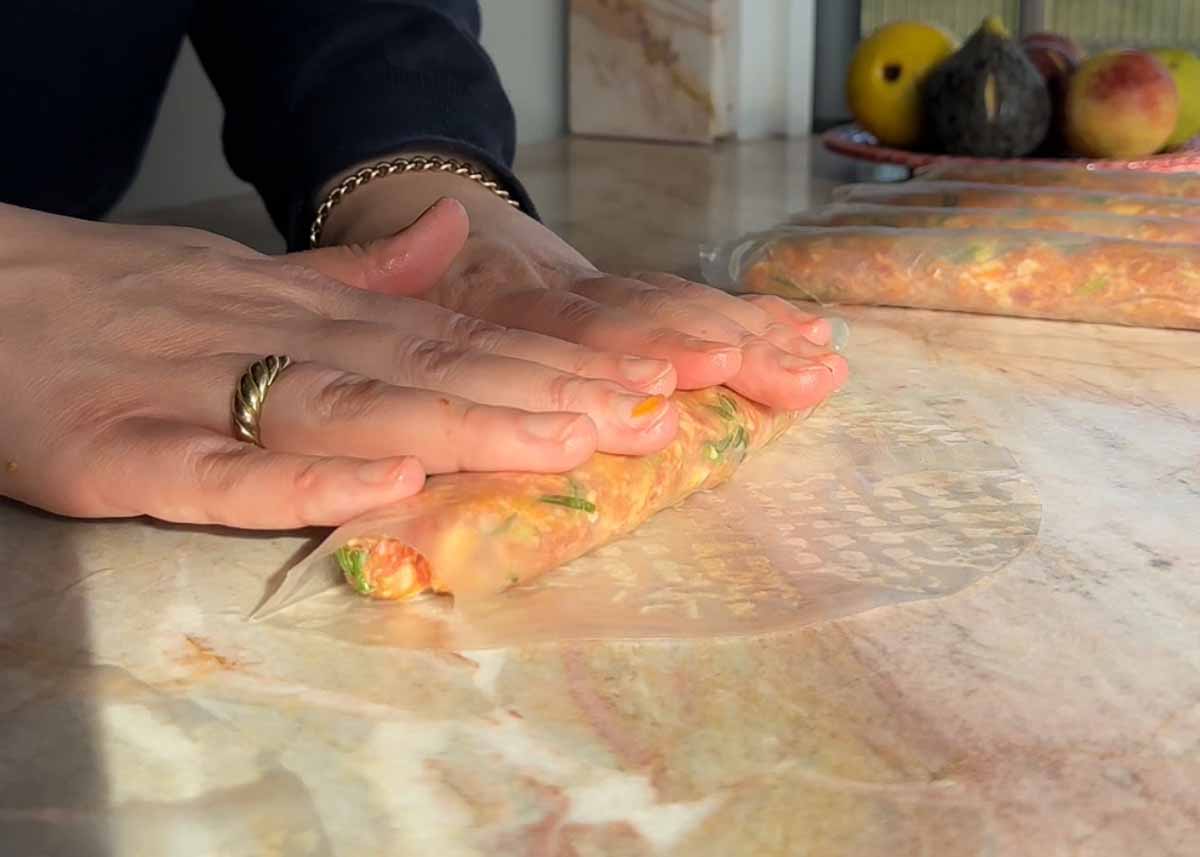Rolling pork filling tightly into softened rice paper to form a dumpling log.