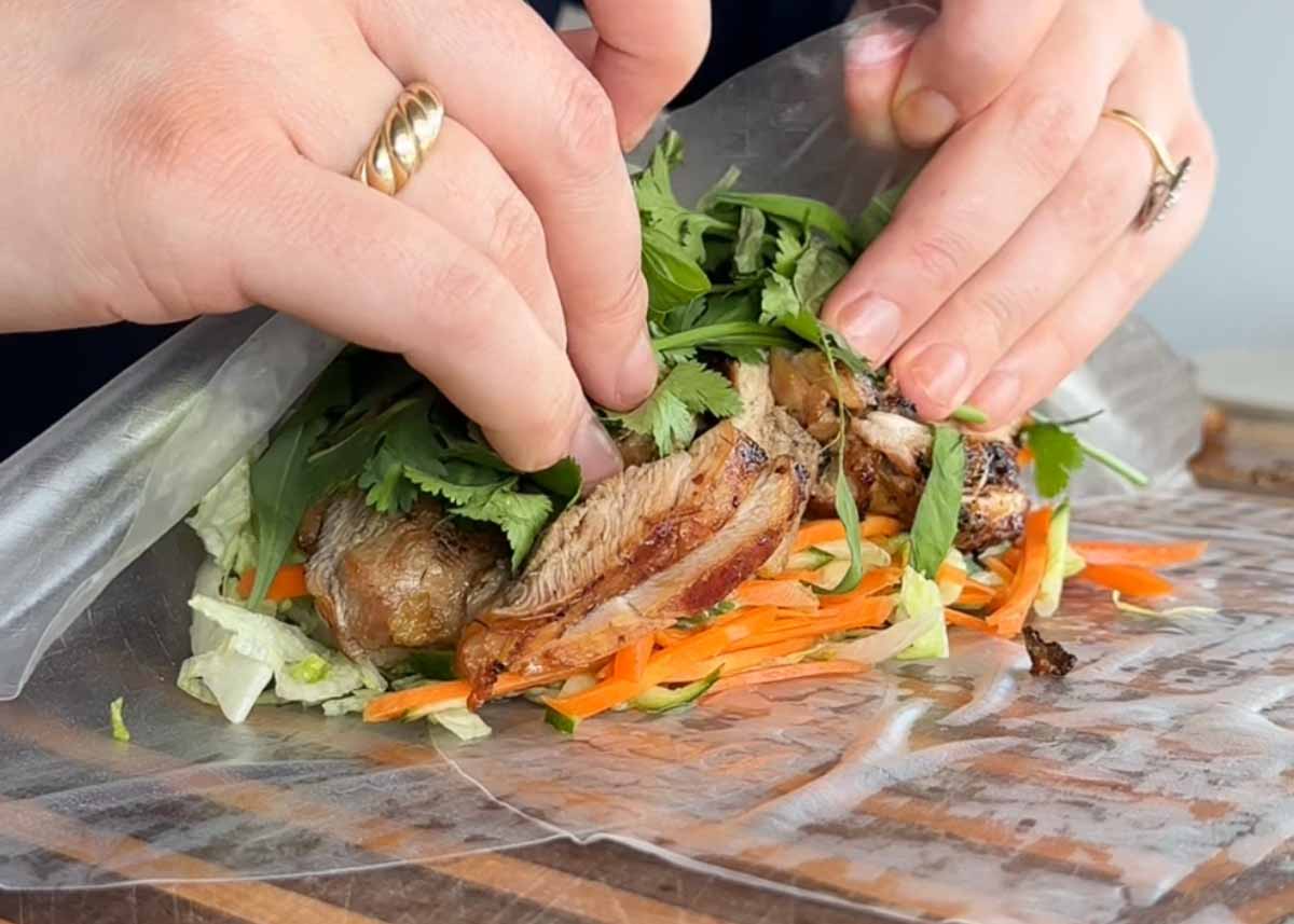 Rolling a lemongrass chicken rice paper burrito with herbs and pickled vegetables.