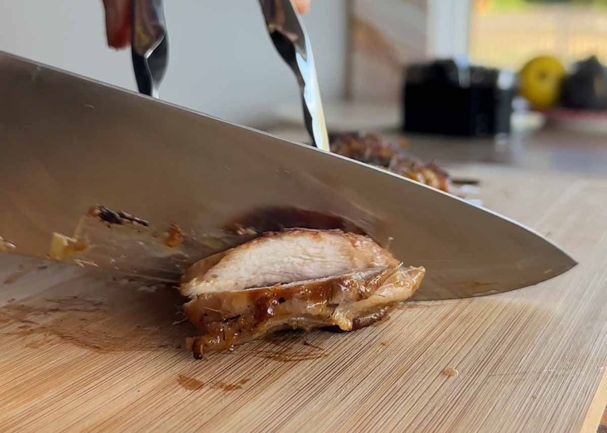 Slicing cooked lemongrass chicken on a chopping board.