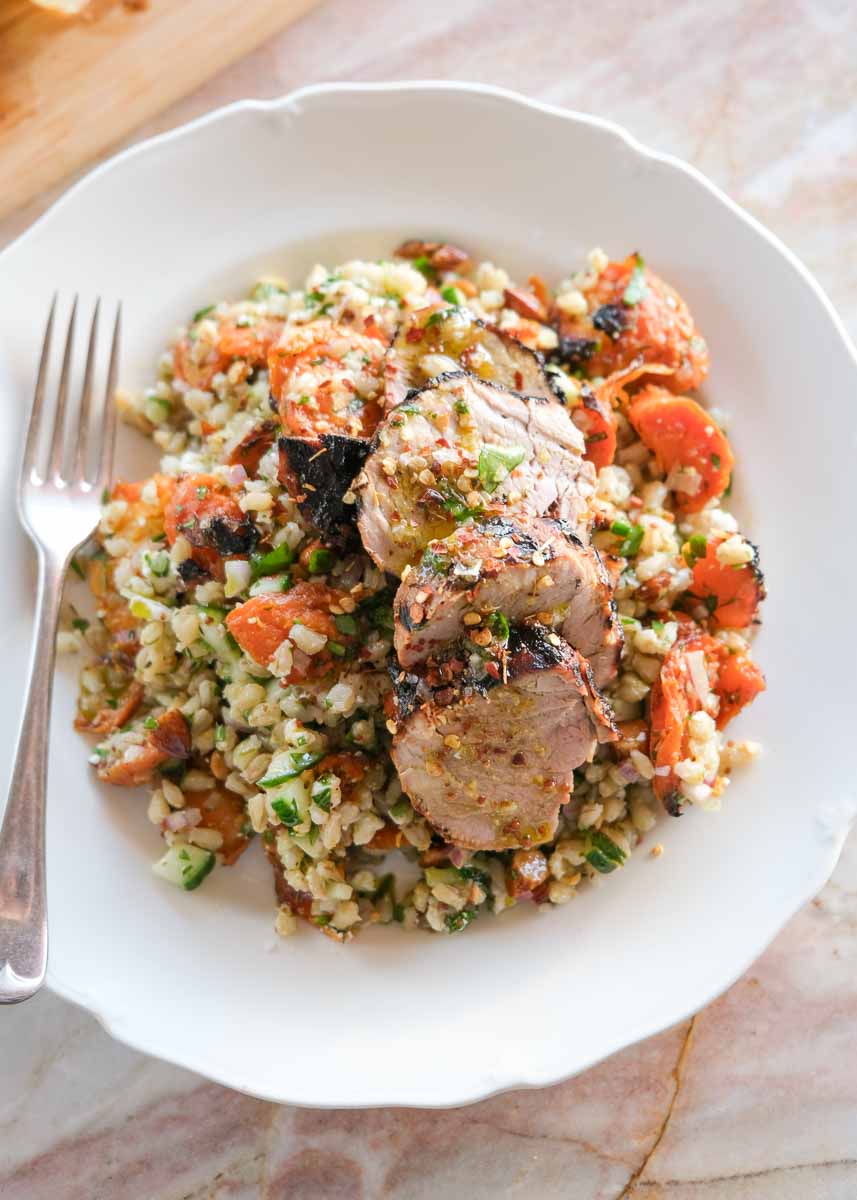 Close up of sliced honey mustard pork served over smashed roasted carrot and pearl barley salad with feta and herbs.