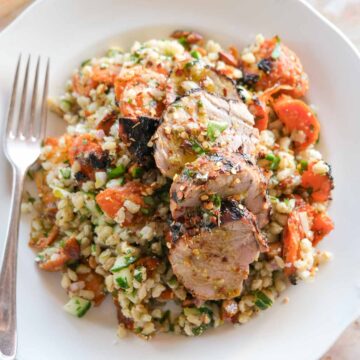 Bowl of smashed carrot salad with pearl barley, feta, herbs and sliced honey mustard pork tenderloin on top.