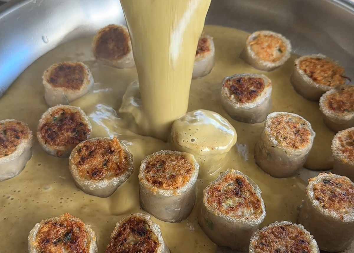Pouring creamy green Thai curry sauce over crispy chicken rice paper dumplings.