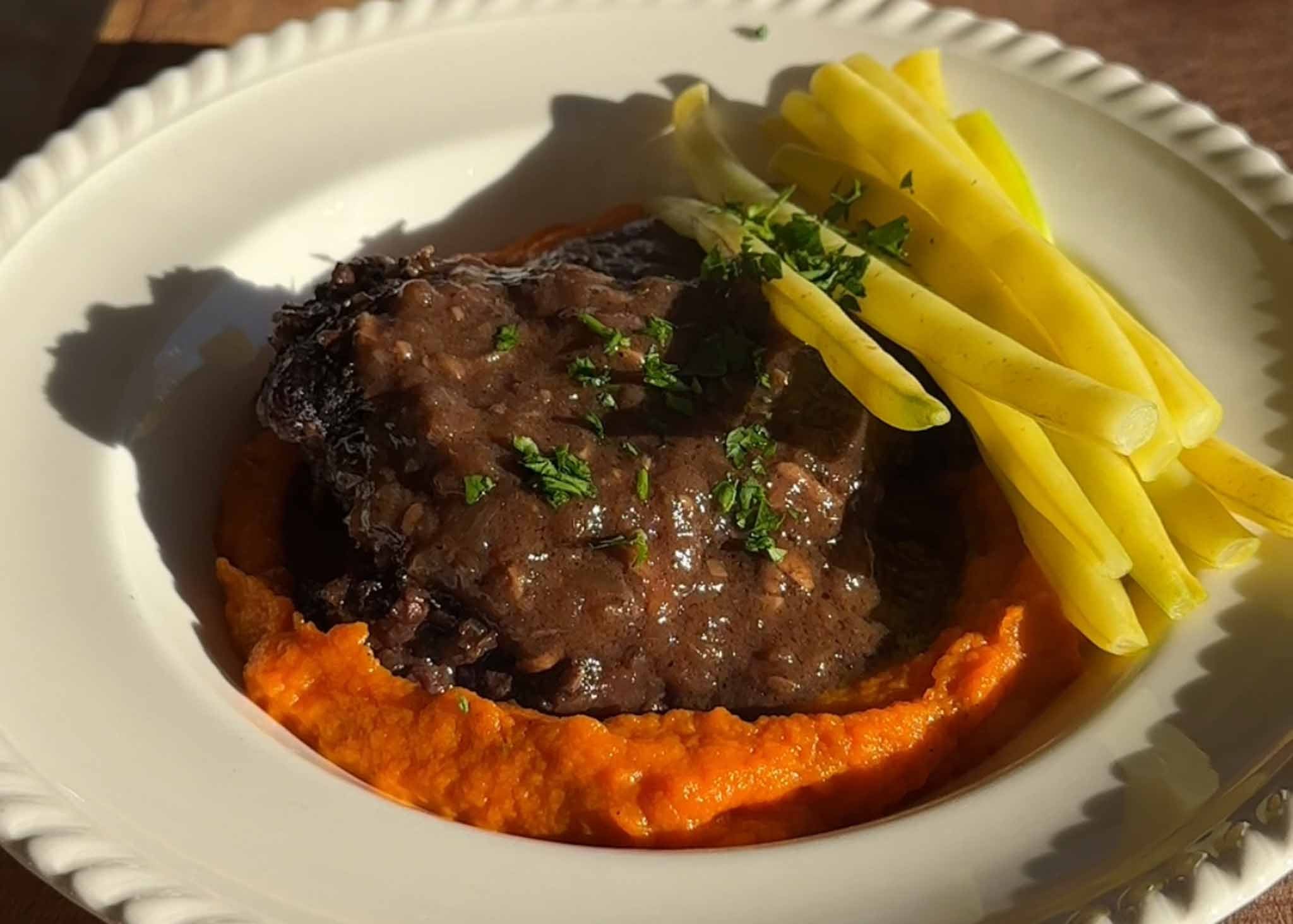 Slow-braised beef cheeks plated with smooth carrot purée and green beans