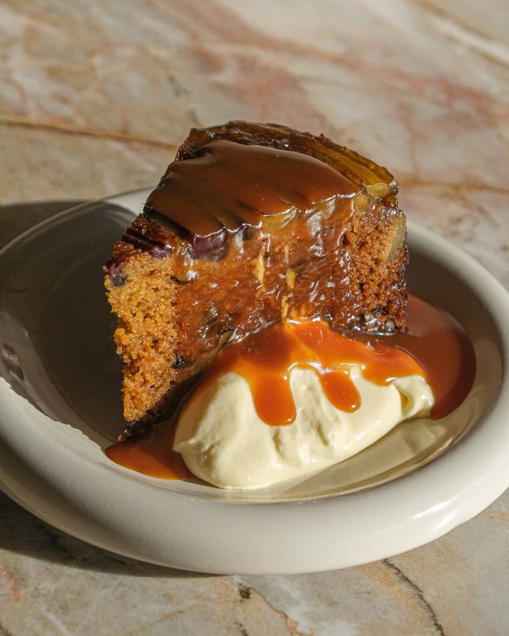 Slice of caramel upside-down carrot cake served with whipped cream cheese and caramel sauce