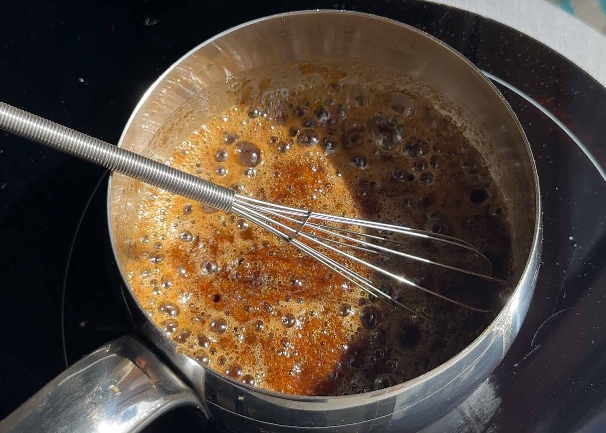 Homemade caramel sauce being whisked in a saucepan