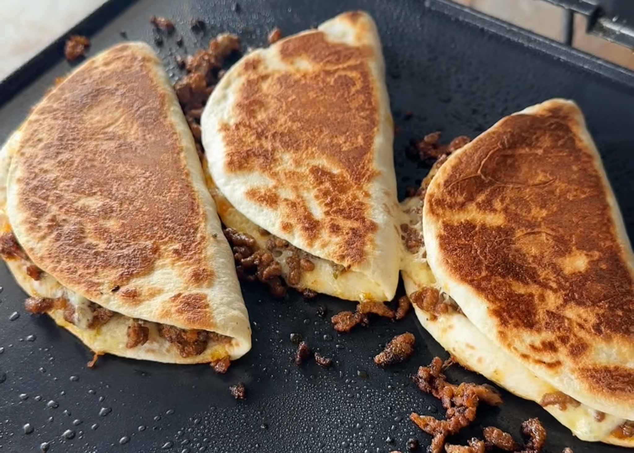 Beef and cheese tacos cooking in a frying pan until golden and crispy