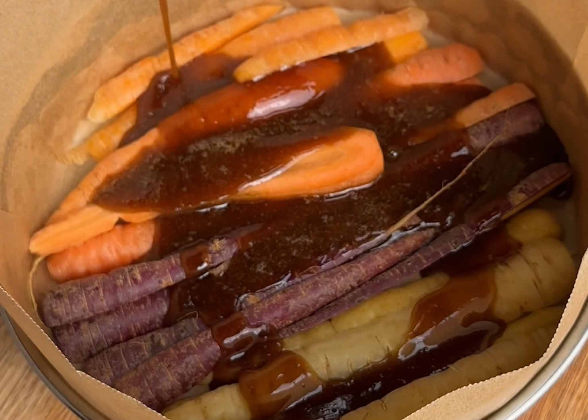 Caramel sauce poured over heirloom carrots in a lined cake tin