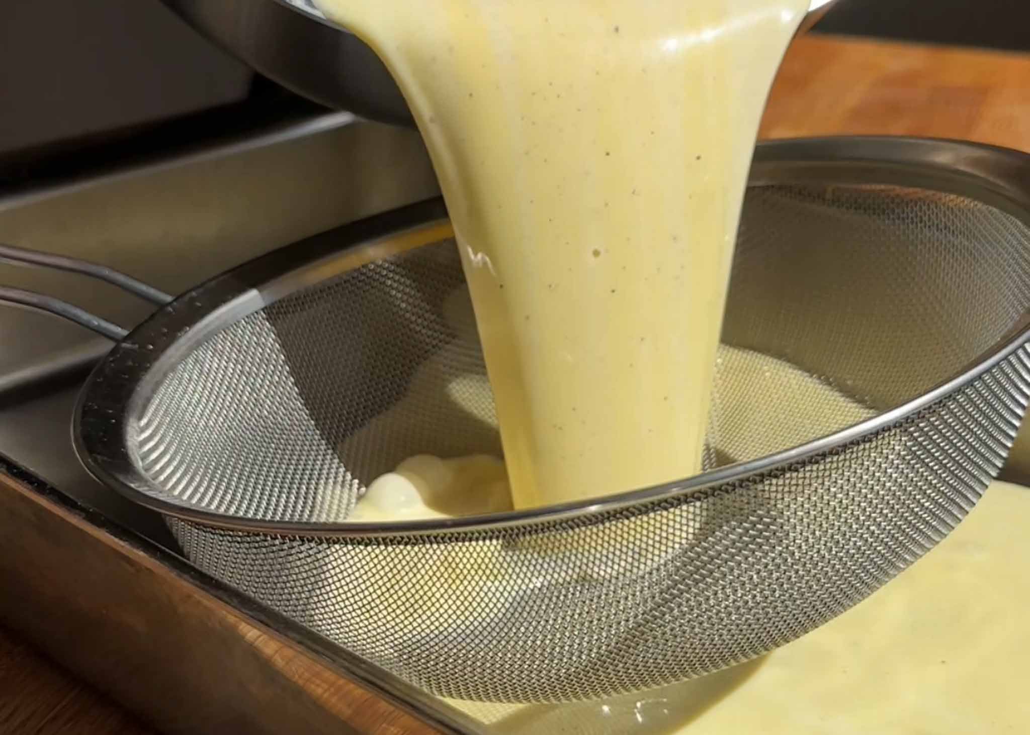 Homemade ice cream custard being poured through a fine mesh sieve