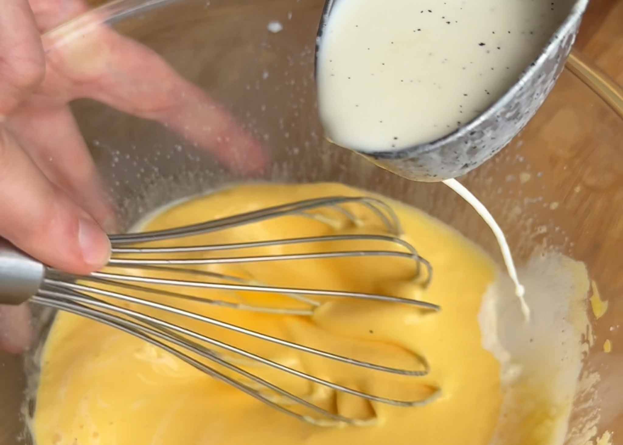 Warm cream being whisked into egg yolks to temper them